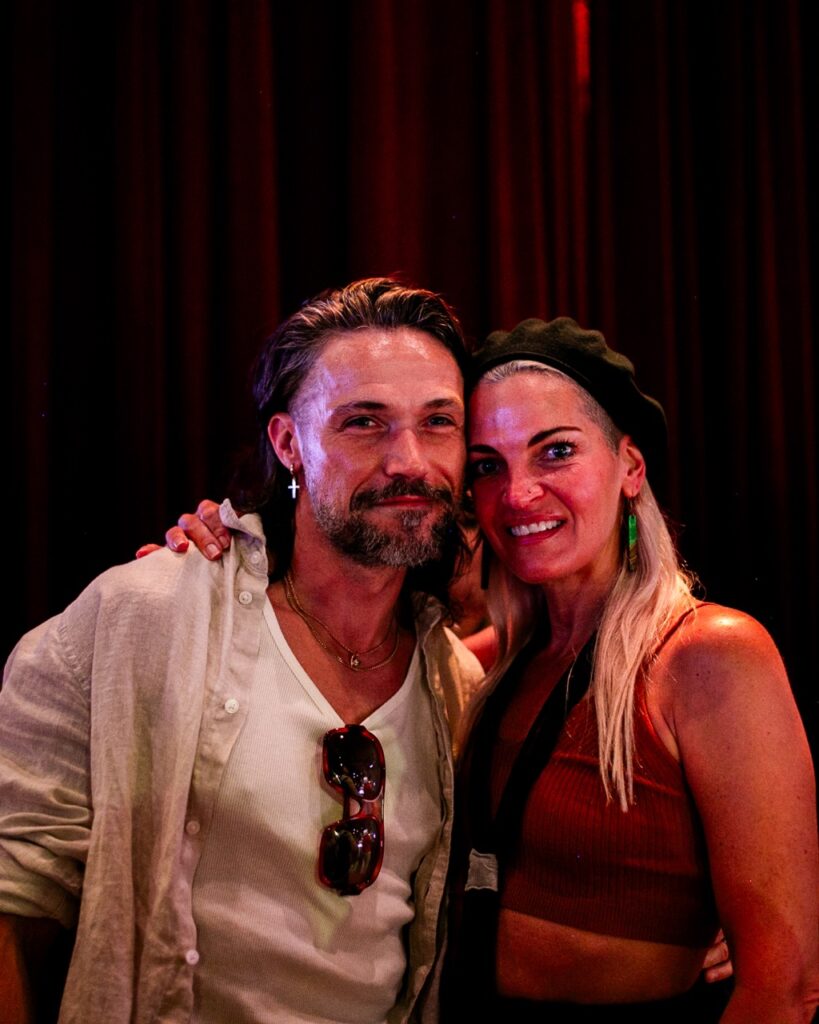 A woman and man stand together against a red curtain.