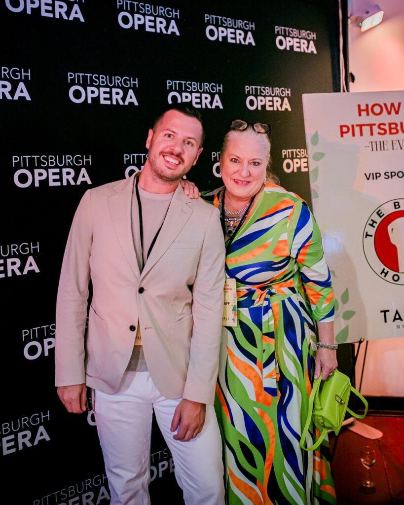 A man in a beige suit jacket and a woman in a green and orange dress stand together.