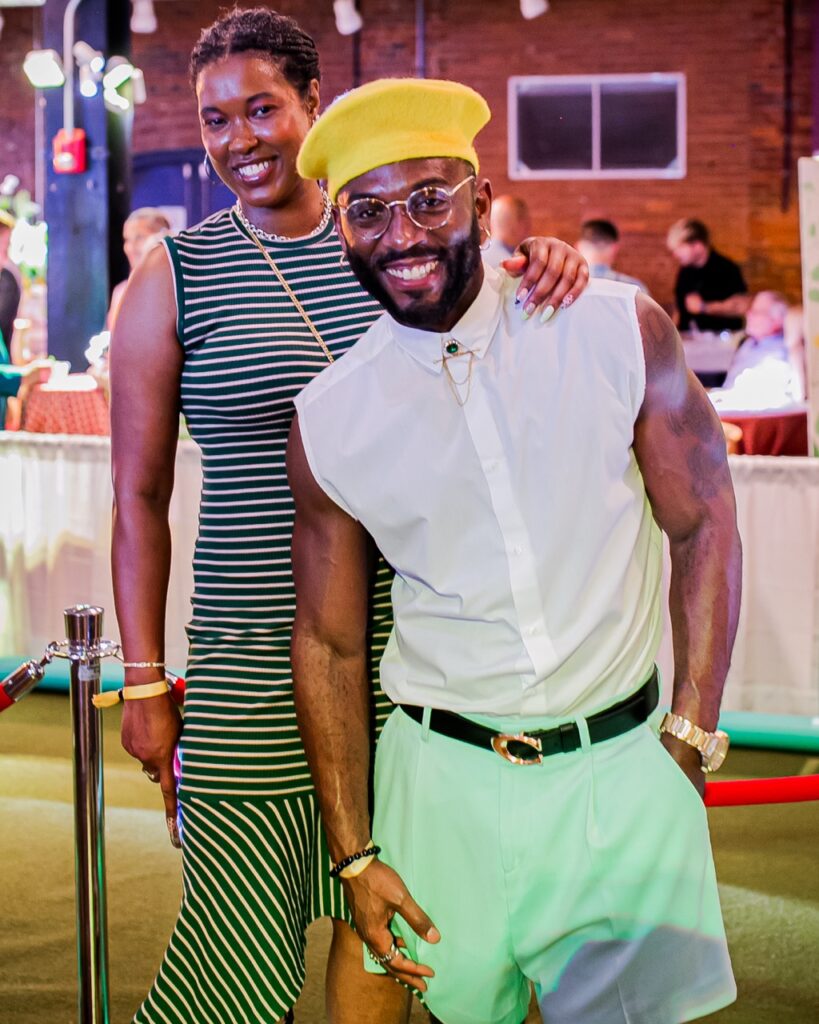 A man in a yellow beret stands with a woman in a striped dress.