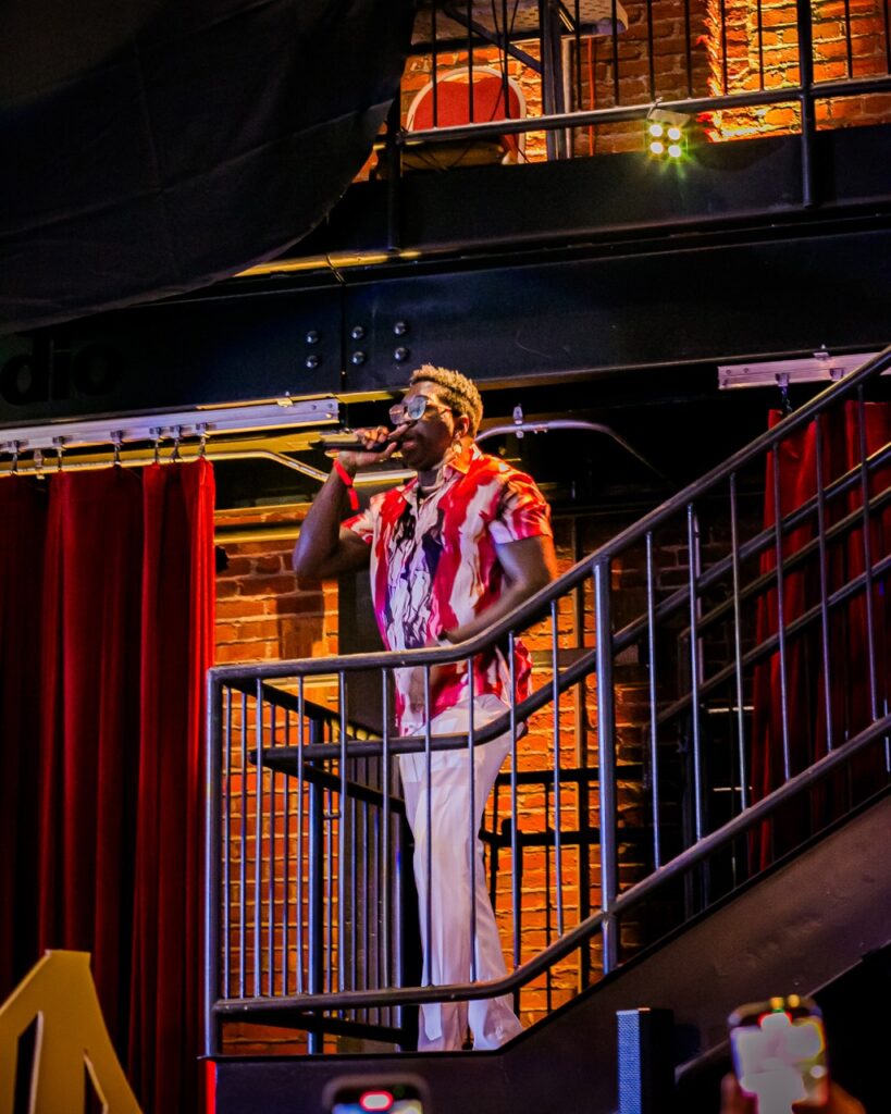 A man sings on a balcony in a red and white shirt.