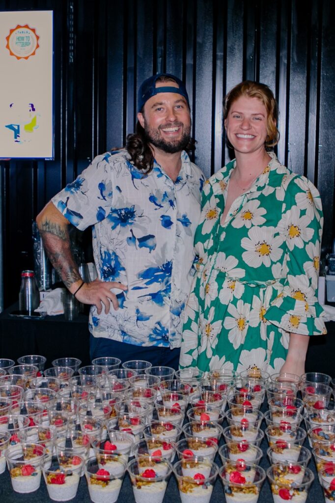 A man in a blue floral shirt and a woman in a green and white flower dress stand together.