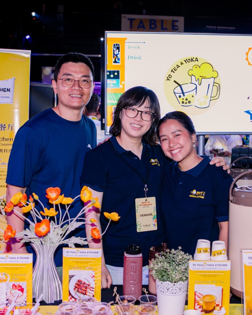 A group of three people stand together in front of the Yo Tea and Yoka sign.