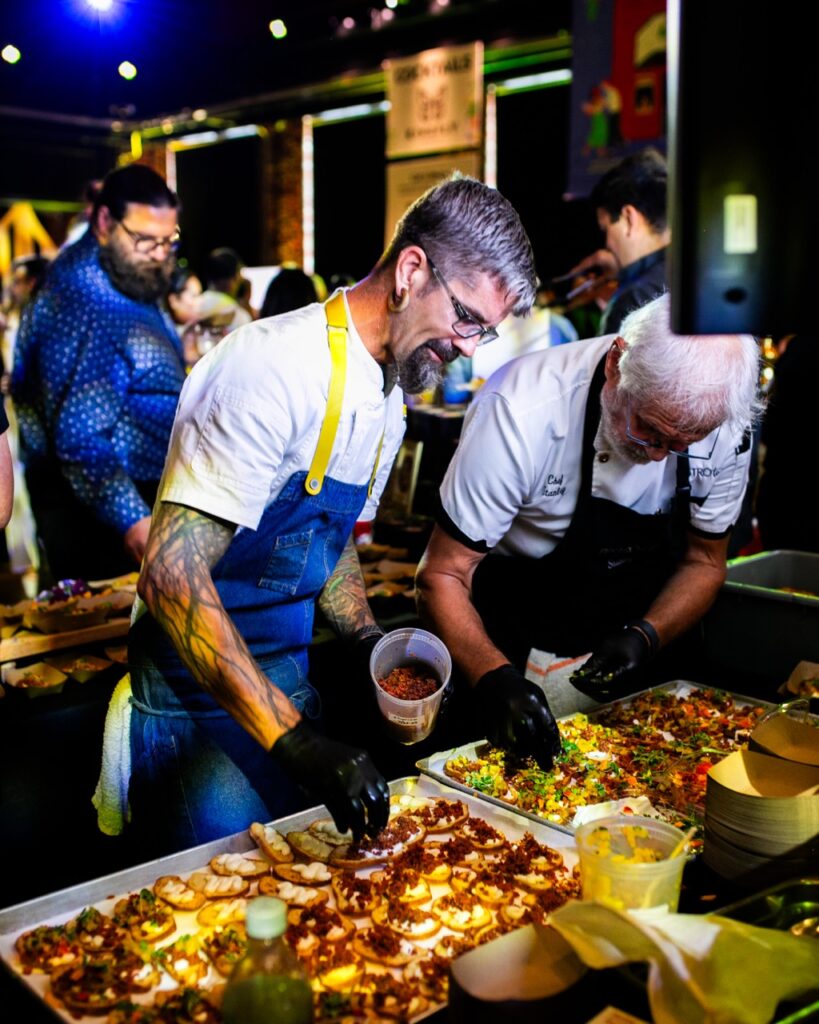 Two chefs dress small slices of bread with different ingredients.