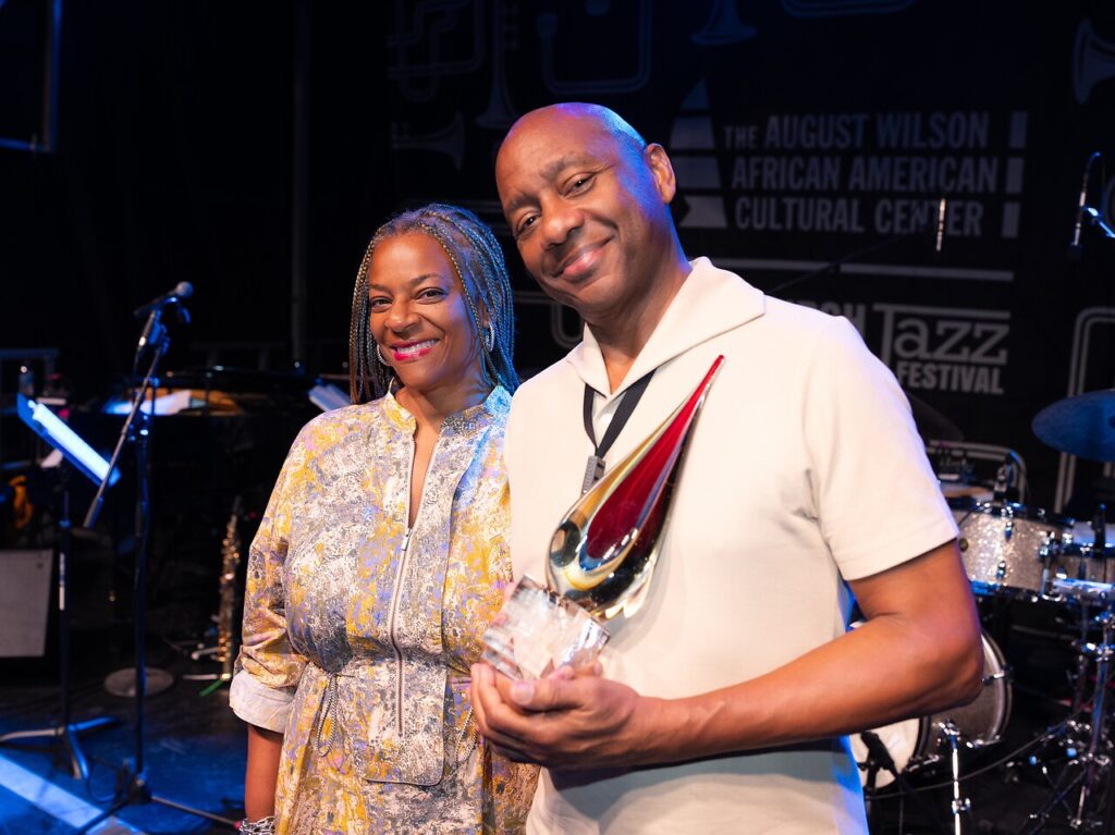 A man with an award stands beside a woman in a dress.