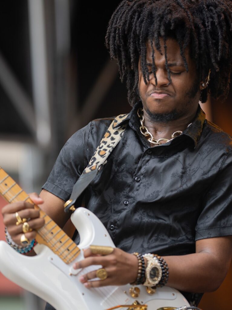 A man plays a white guitar with a cheetah print strap.