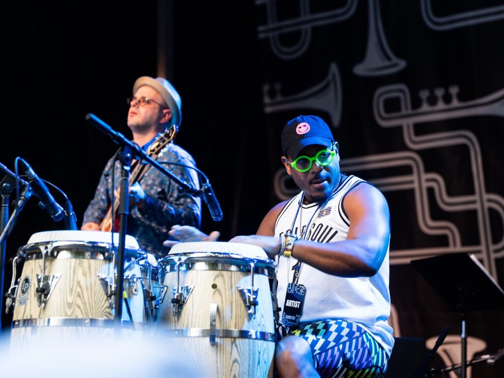 A bongo player and guitar player jam on stage.
