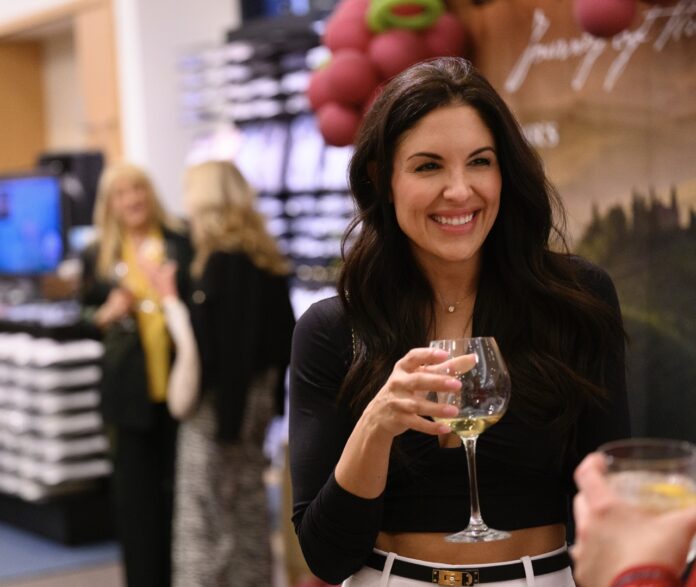 A woman in a black long sleeve holds a wine glass, smiling.