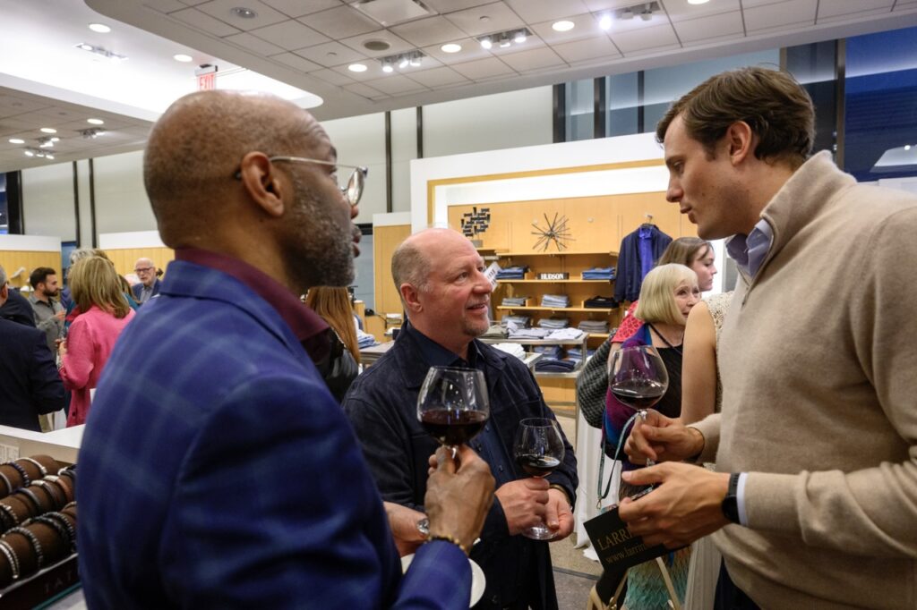 Three men holding wine glasses talk with each other.