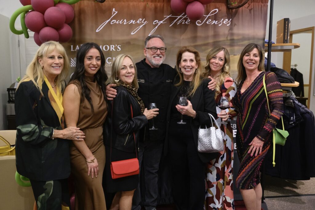 A group of women stand around a man with black glasses.