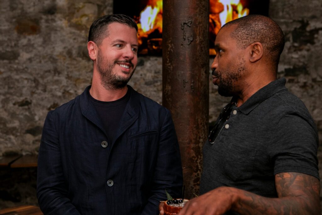 A smiling Justin Matase, a white man with a beard, talking to Jeff Milliner, a Black man with a low haircut, at a non-profit networking mixer.