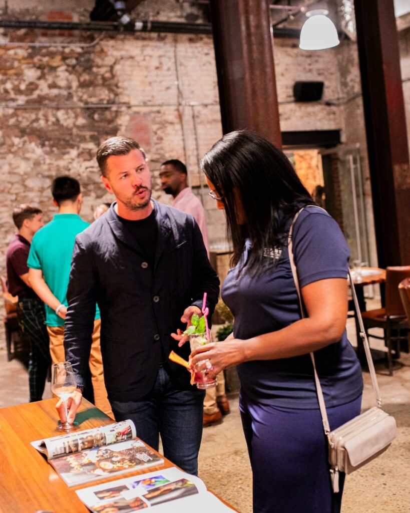 Justin Matase, a man in a dark blazer, talks to Lisa Chester, a woman in a navy polo shirt, at a professional non-profit networking event or mixer.