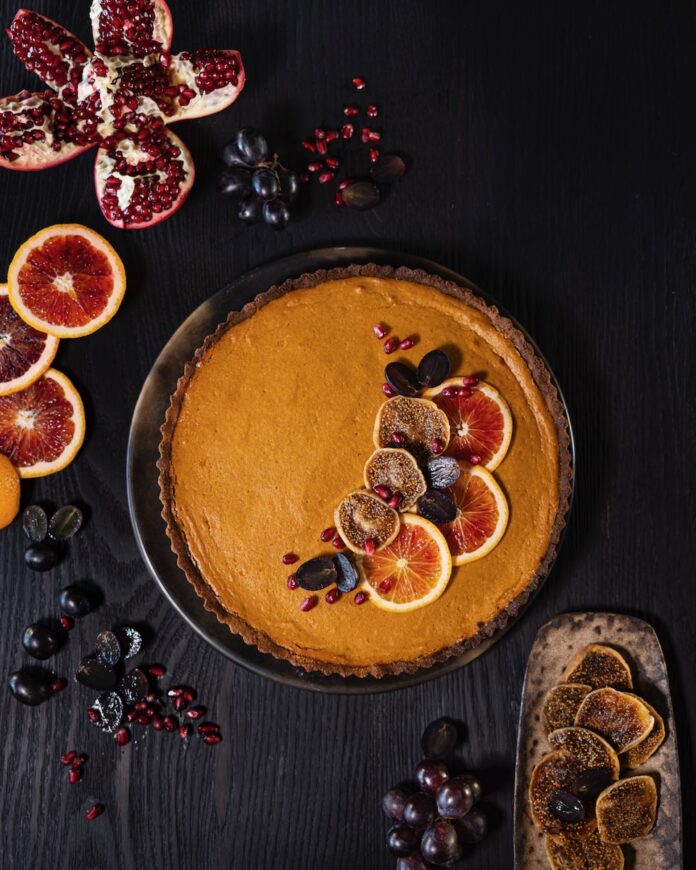Miso Sweet Potato Pie with Grapes TABLE Magazine A miso sweet potato pie sits on a dark wood table with sliced citrus, grapes, and pomegranate seeds on top.