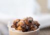 Oliebollen Dutch Donuts A white bowl full of Oliebollen Dutch donuts being held by a person as another sprinkles powdered sugar overtop.