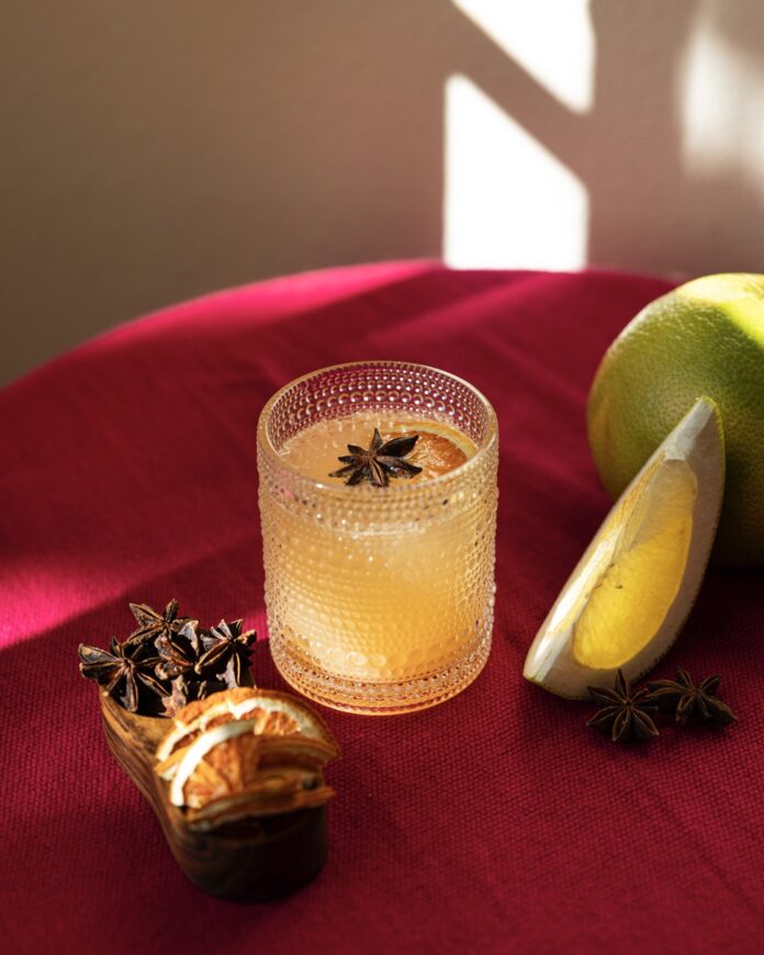  Grapefruit Chai Masala “Mimosa” A chai masala good luck mimosa with grapefruit juice sits on a red table top with a star anise garnish in the glass and citrus slices nearby.