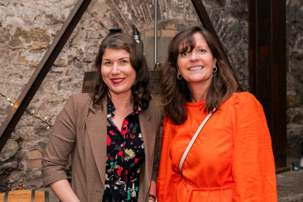 Nicole Lampl and Claire Ertl smiling together in front of a stone wall at a professional non-profit networking mixer.