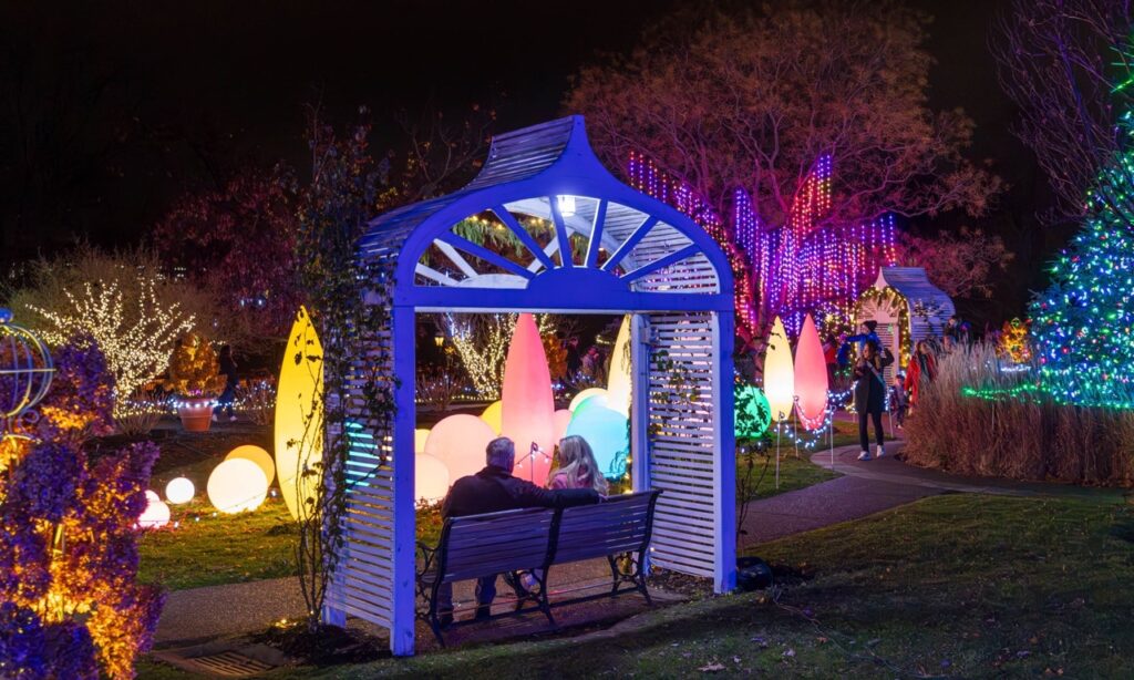 A couple sits under a white arch with lights in the background.