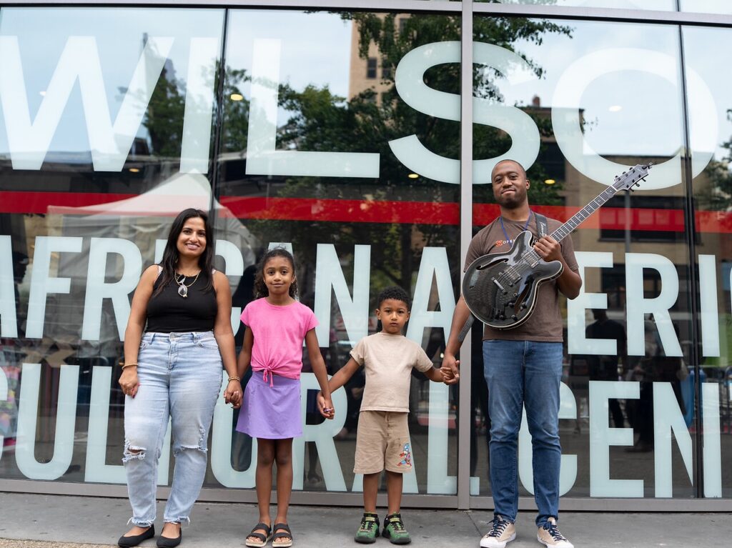 A mom and dad with a guitar stand with their kids between them.
