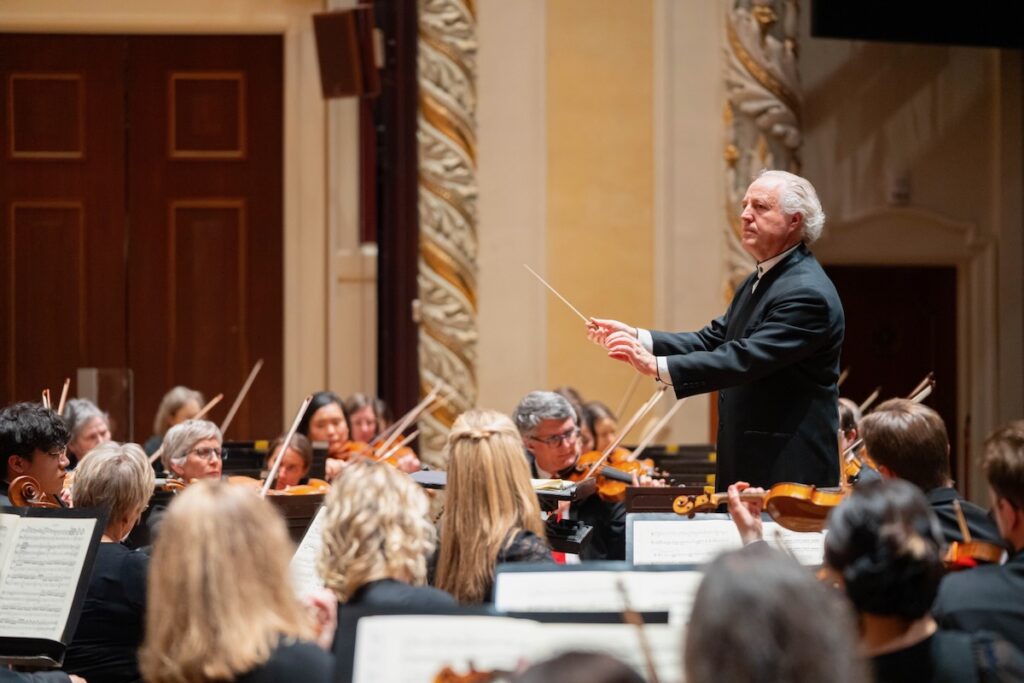 A man in a black suit conducts the Pittsburgh Symphony Orchestra.