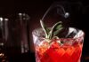 Pomegranate Boulevardier A Pomegranate Boulevardier cocktail in a cut crystal glass, garnished with a smoking sage sprig and ice, with dried petals and a pitcher in a dark, moody setting.