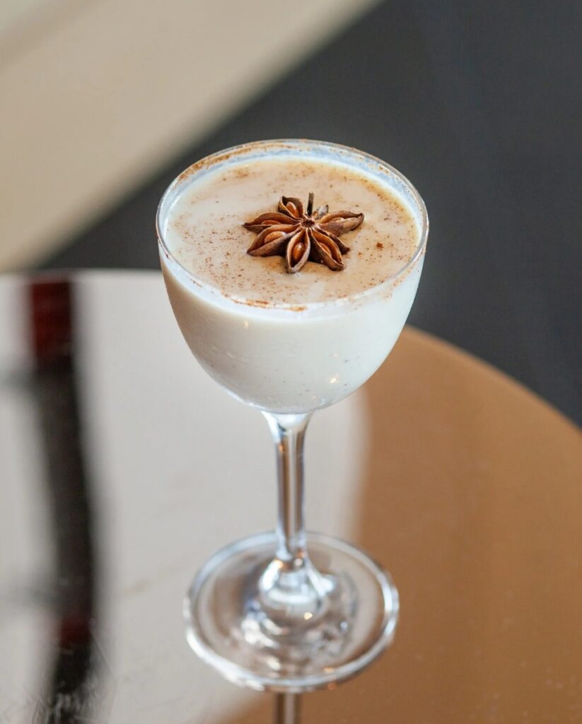 A chilled Coquito cocktail in a coupe glass, garnished with a star anise and cinnamon, for a Puerto Rican holiday drink.