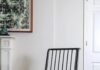 Pittsburgh Regional Reuse/Recycle/Repair Heroes A black spindle-back armchair with a thick white sherpa cushion sits in a minimalist room with a decorative white fireplace mantel, a modern side table, and a neutral geometric rug, highlighting furniture refinishing and antique restoration.