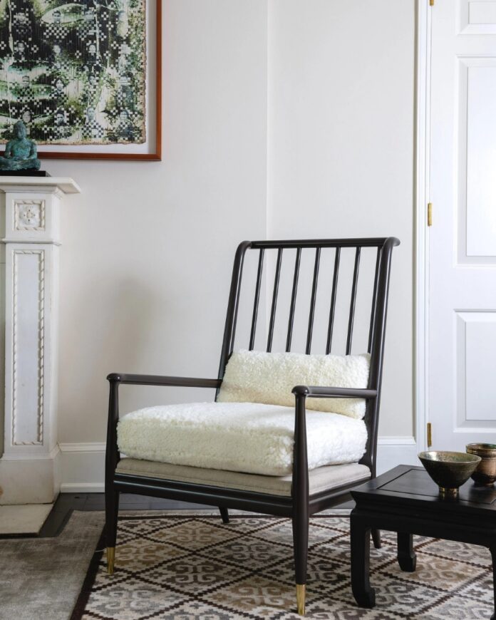 A black spindle-back armchair with a thick white sherpa cushion sits in a minimalist room with a decorative white fireplace mantel, a modern side table, and a neutral geometric rug, highlighting furniture refinishing and antique restoration.
