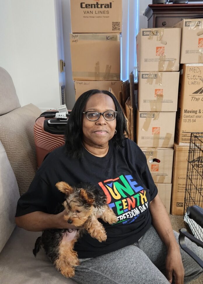A woman sits on a couch with a dog in her arms.