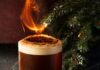 4 Winter Cocktail Recipes for Sharing with Friends and Family A Smoked Vanilla Carajillo cocktail in a rocks glass with a layer of foam and a burning, cinnamon-dusted orange peel garnish, set next to a pine garland.