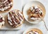 Confectionary Masters and Local Bakeries in Pittsburgh Round mini chocolate tarts with flaky crusts, topped with whipped cream, chocolate drizzle, and chopped nuts, with one tart cut into pieces on a small white plate for serving.