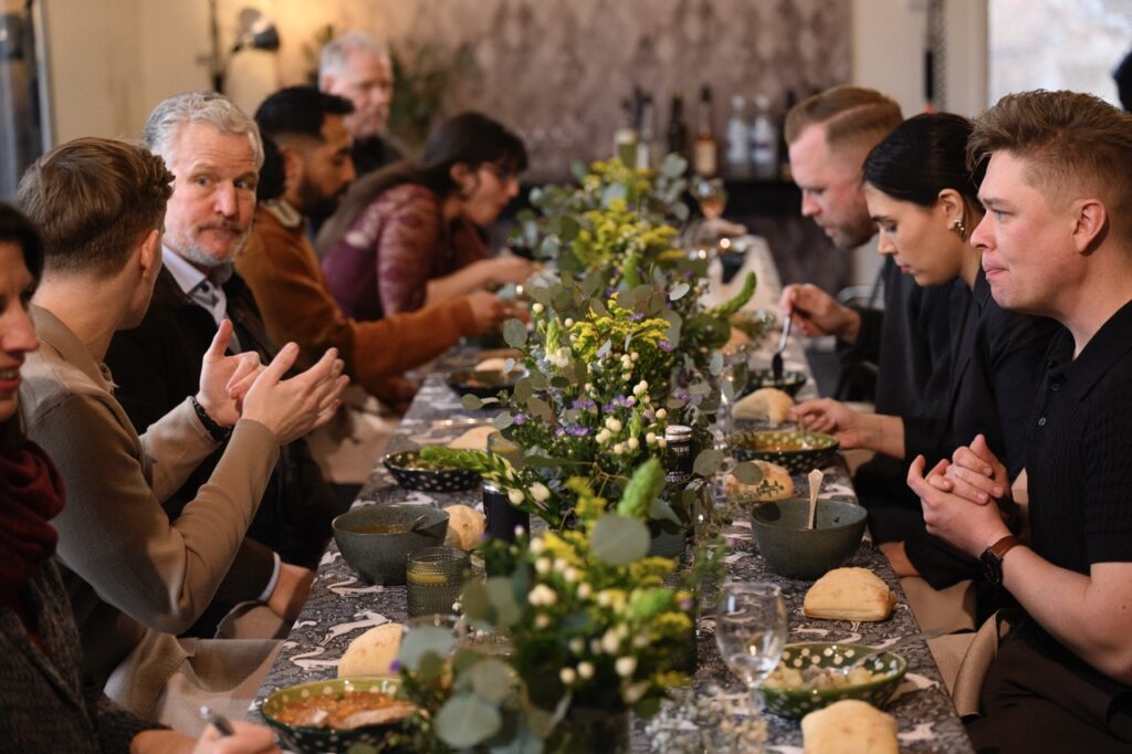 People on both sides of a long table dive into bowls of soup.