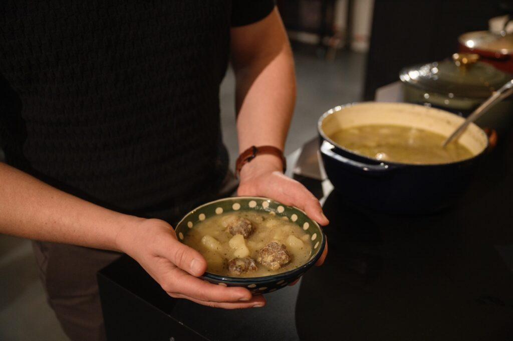 A man holds a bowl of dumpling and meatball soup in his hands.