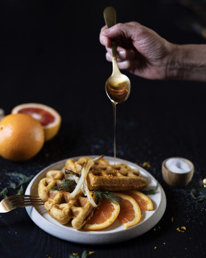 Sweet Potato Waffles A stack of sweet potato waffles with citrus slices and a drizzle of honey over top.