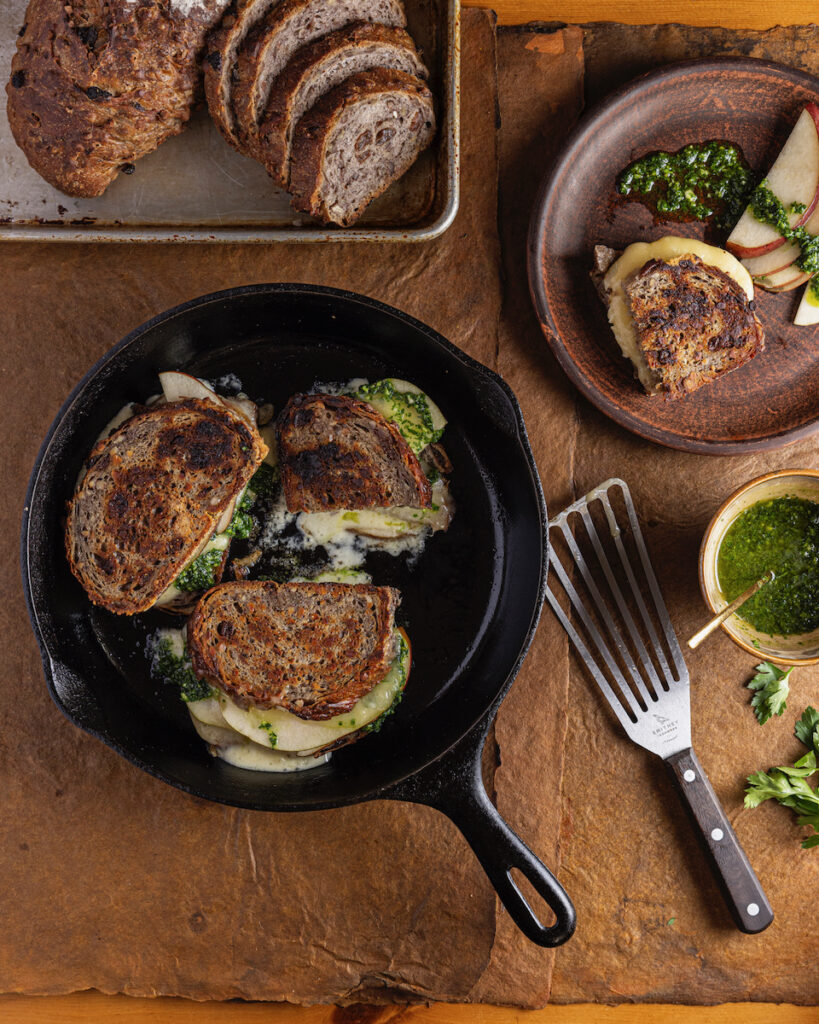 A pear grilled cheese sandwich set on a rustic table with slices of bread beside it