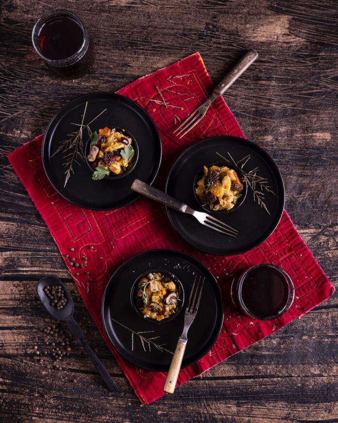The Ultimate Stuffing Recipe Three black bowls hold three servings of stuffing with forks inside each bowl and a red cloth below the bowls.