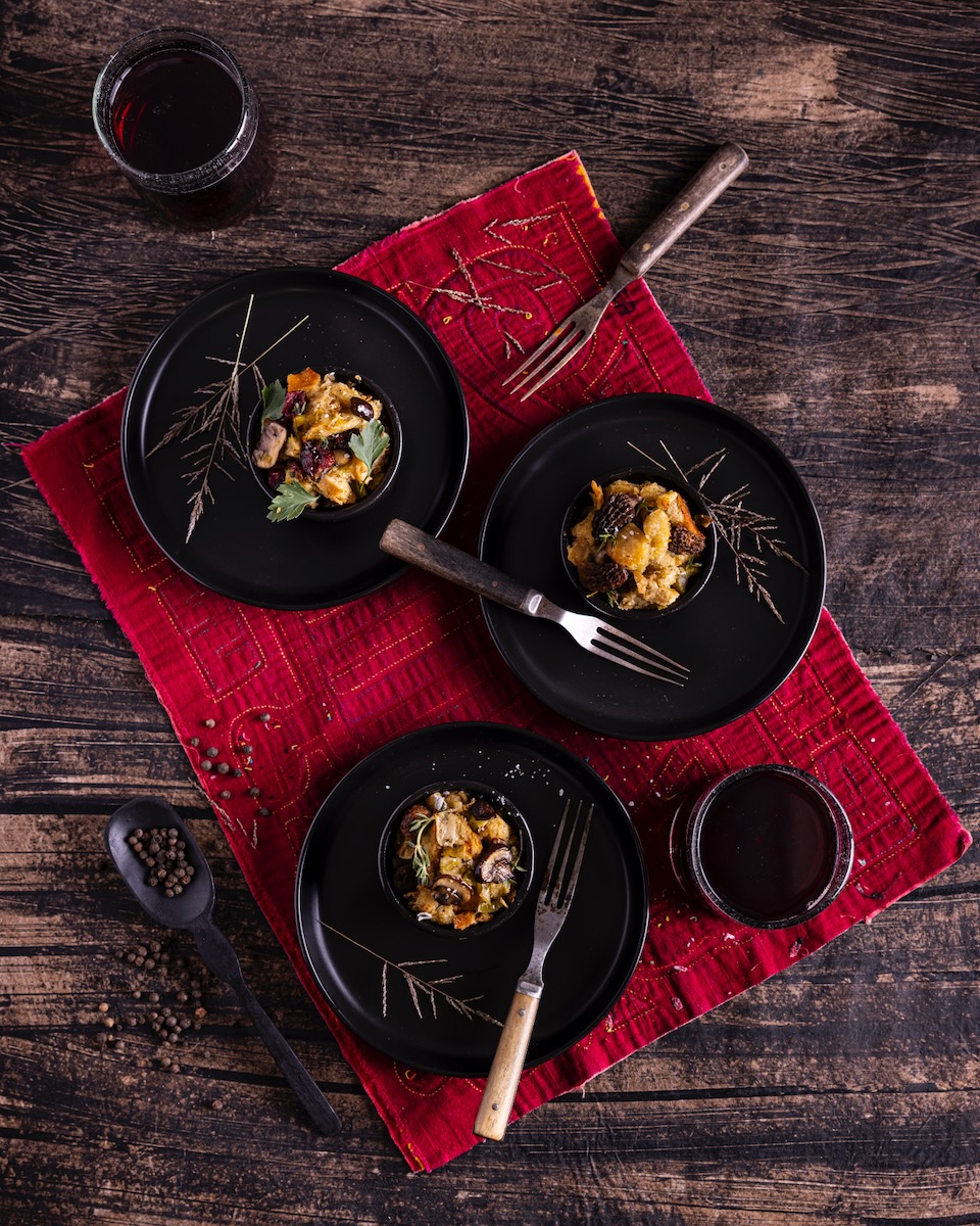 Three black bowls hold three servings of stuffing with forks inside each bowl and a red cloth below the bowls.