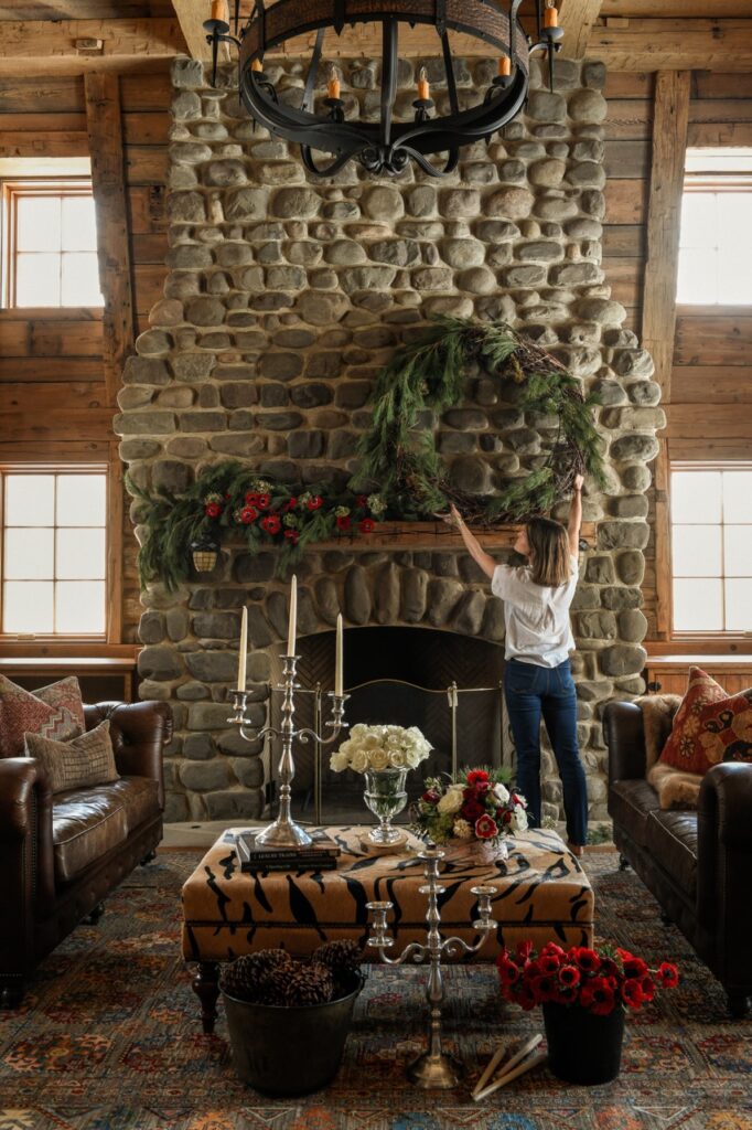 A woman decorates a stone fireplace with a large green wreath.