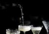 Best Bubbly Bottles for New Year’s Eve A person pours sparkling wine for New Year's Eve into four tall glasses on a table table.