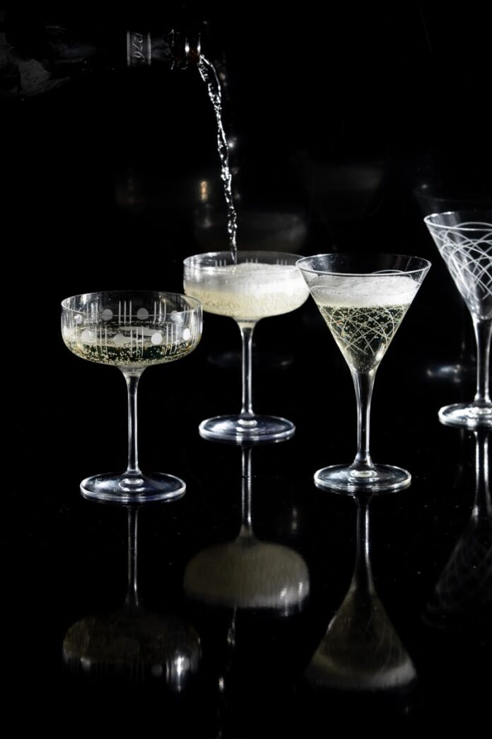 A person pours sparkling wine for New Year's Eve into four tall glasses on a table table.