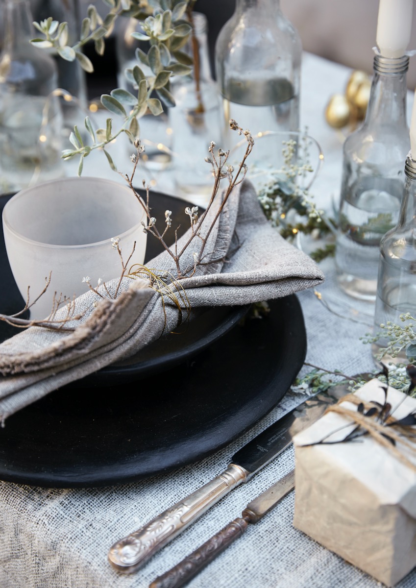 A small white cup set on a table with napkins and small twigs for Christmas decoraition