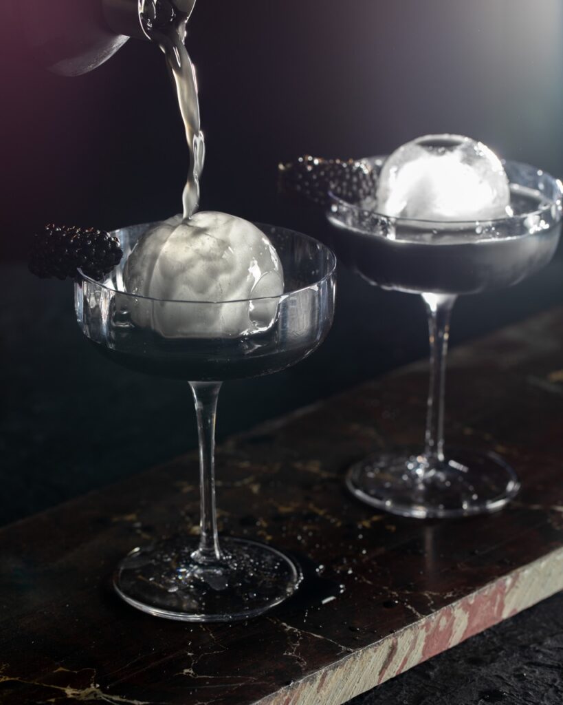 Water pours over an ice ball in a martini glass.