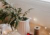 Best Gifts For Hard-to-Shop-For People A brown wrapped gift sits on a white cloth table with a plaid hanker-chief beneath it and a pine branch in a ceramic pitcher.
