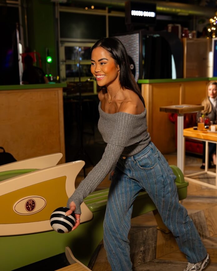 Stay Out of the Cold at Indoor Activities in Pittsburgh for Adults A woman bowls a small bowling ball down a lane in a grey sweater and jeans.