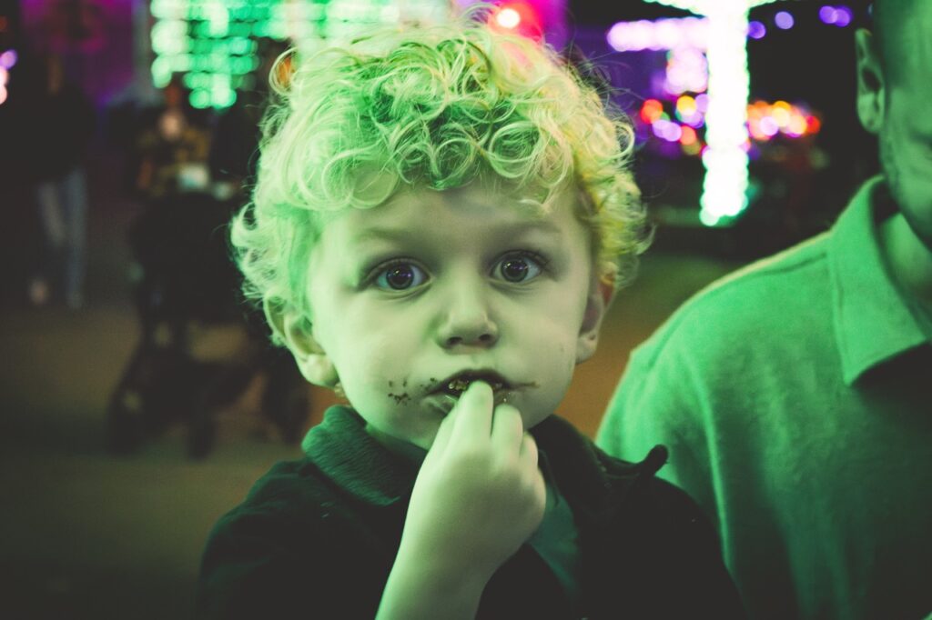 A young boy looks at the camera with food in his mouth.