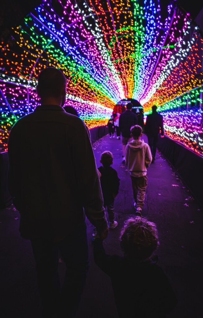 A family walks through a rainbow tunnel of lights.