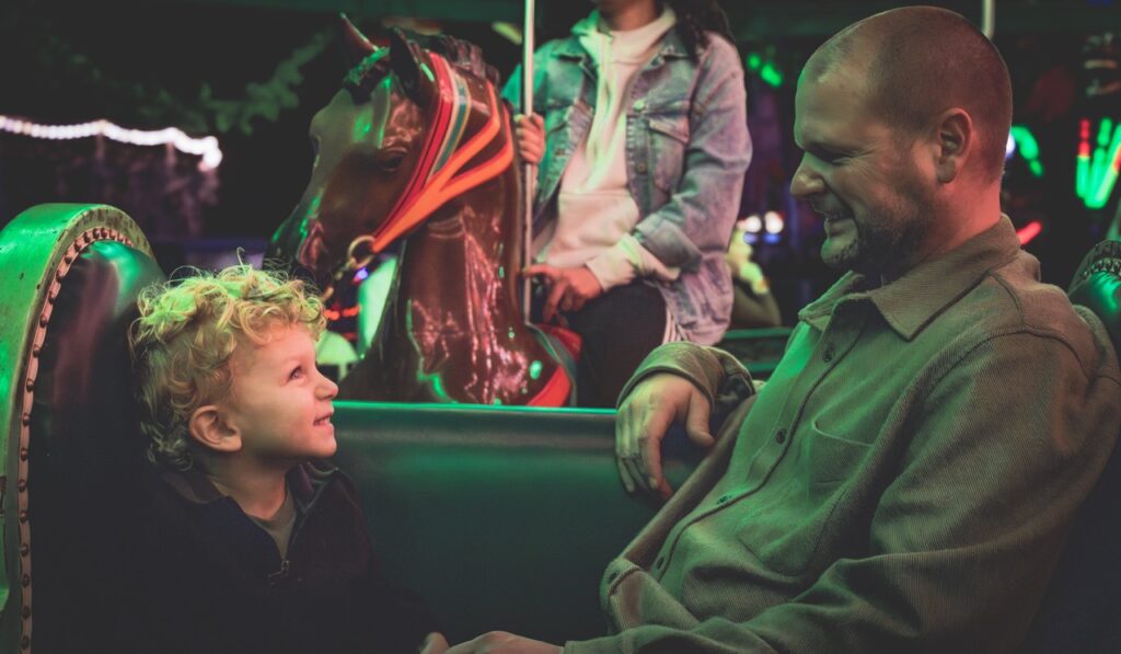 A dad and his son smile at each other on a bench.