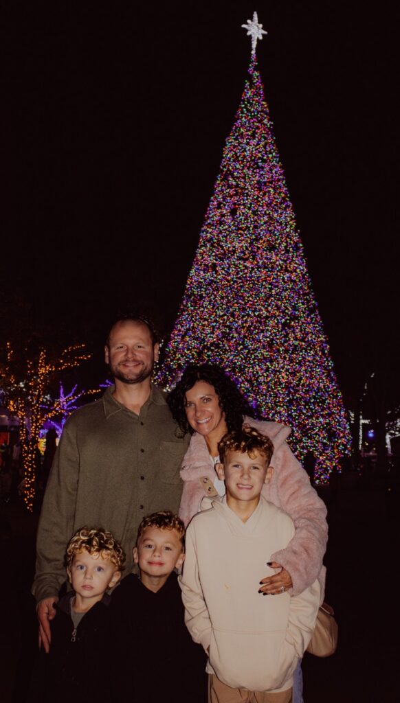 A family stands in front of a Christmas tree lit in Rainbow lights.
