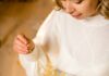 Last Minute Gifts for Holiday Hosts and Hostesses A woman sits on the floor, opening a white present with a gold bow.