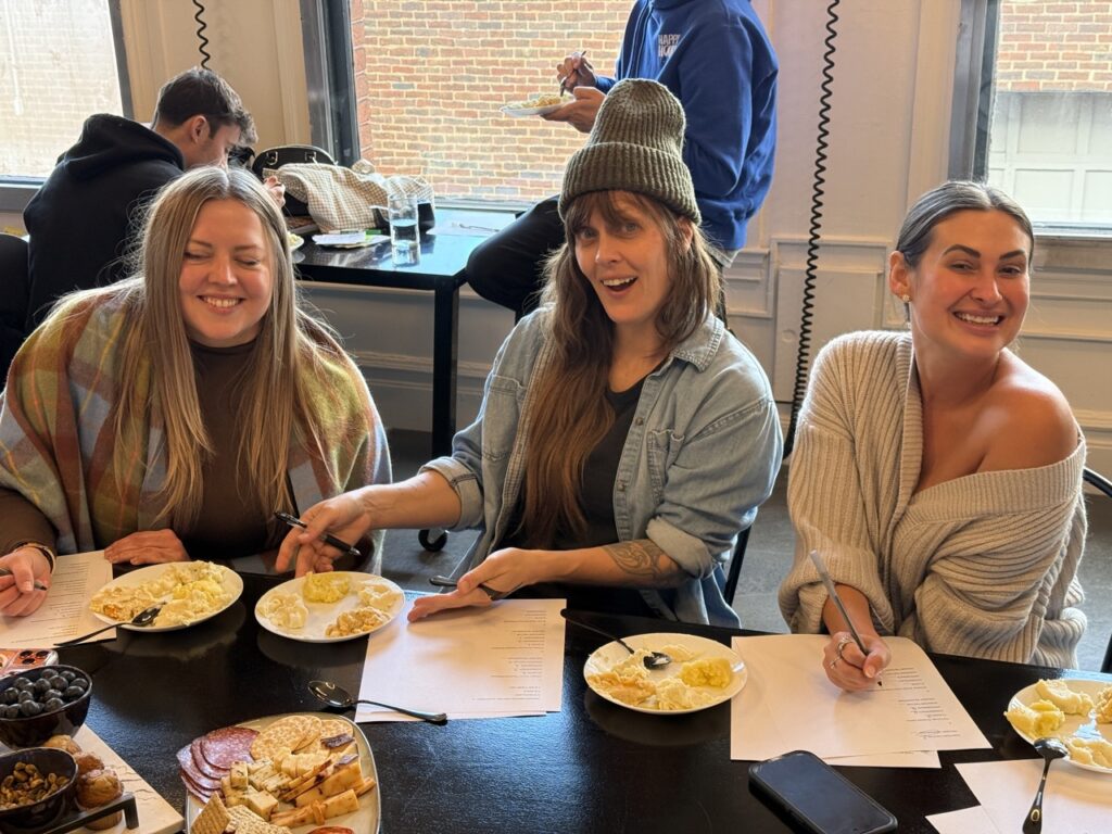Three women sit at a table with papers and plates.