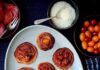 Pancake Pizzas Seven mini pancake pizzas topped with tomato sauce, melted cheese, and halved cherry tomatoes on a light gray oval platter, surrounded by bowls of pepperoni slices, parmesan cheese, and grape tomatoes.