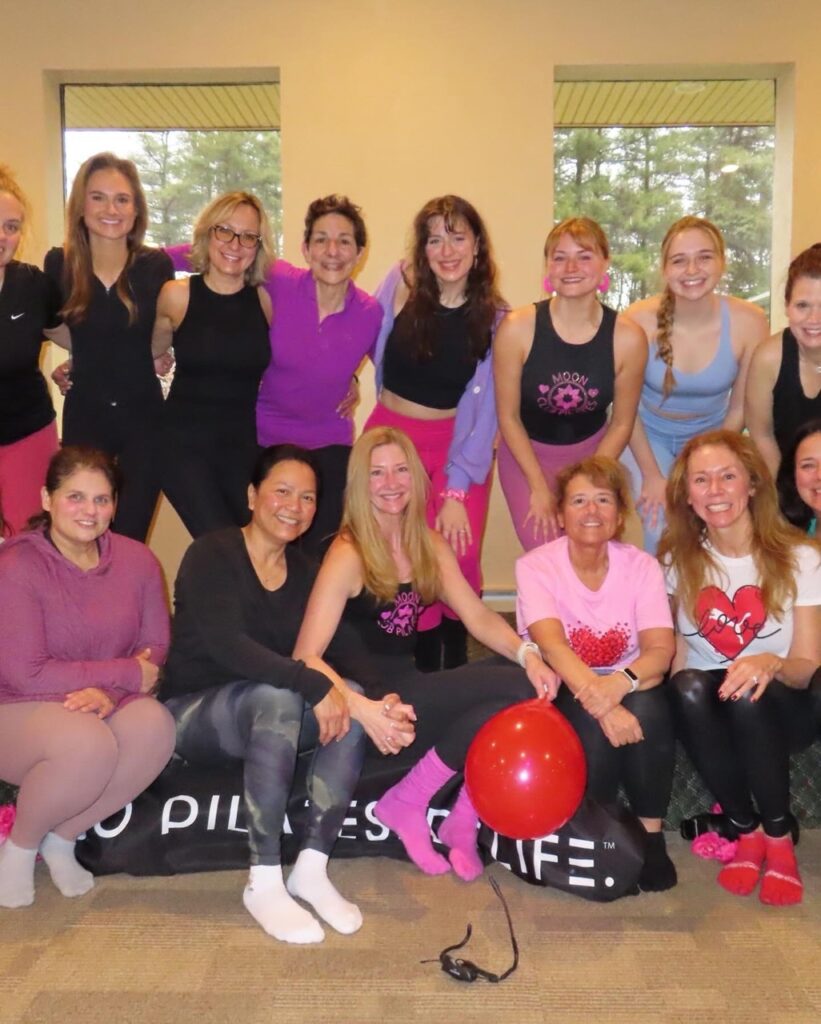 A group of women sit and stand together in a gym space.